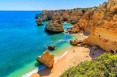 Steile Küste und feiner Sandstrand treffen auf blaues Meer.