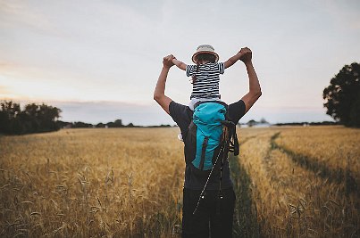 Vater mit Tochter auf den Schultern wandert durch ein Feld