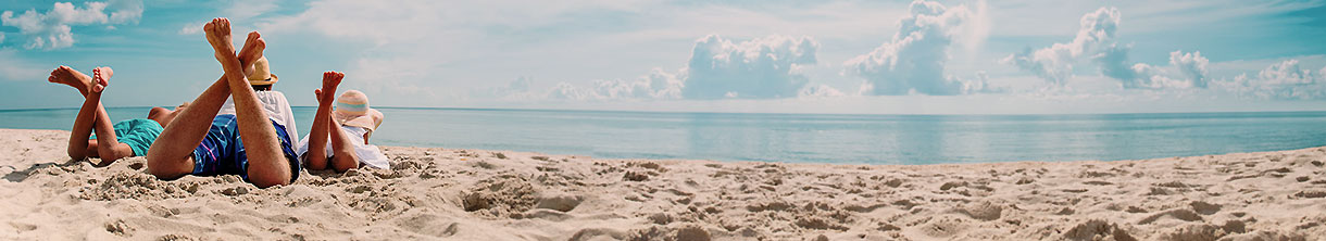 Vater mit zwei Kindern liegt am Strand. 