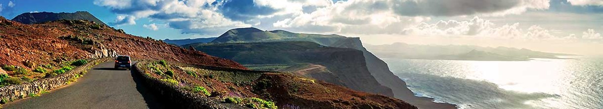 Auto fährt über einsame Küstenstraße in Vulkanlandschaft.